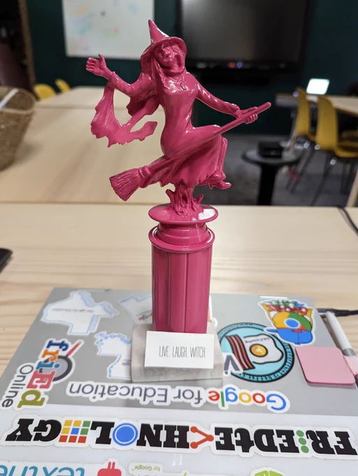 Bubblegum pink, shiny witch trophy on marble base with a sign that says "Live, Laugh, Witch" in Rae Dunn font
