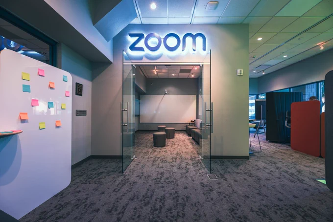 Image of an indoor meeting lab space with chairs, a whiteboard, and a sign of the Zoom logo