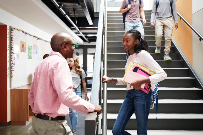 Student standing at bottom of school staircase talking to teacher. 