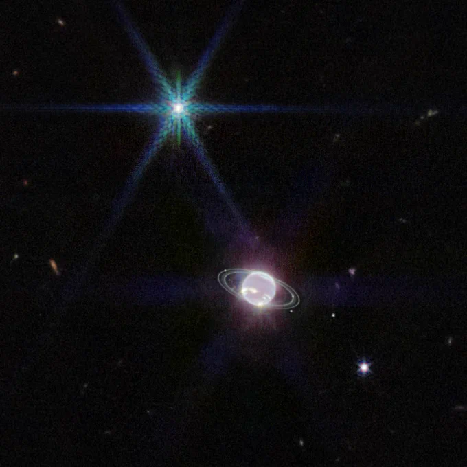 This JWST infrared image is mostly black, with the planet Neptune glowing brightly just below and to the right of the center of the image. Rings are clearly visible around the planet, along with several bright dots: small moons. A very bright dot in the upper left shines in green and blue. This is the bright icy moon Triton.  Credits: NASA, ESA, CSA, STScI