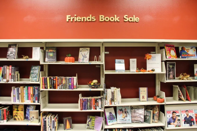A book wall decorated in fall leaves and pumpkins. A sign above the books reads "Friends Book Sale."