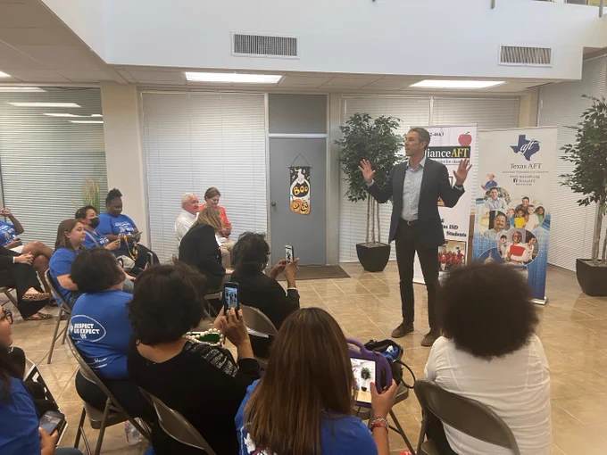 Beto stands in front of a group of seated educators and gestures with both hands. Behind him are Alliance A-F-T and Texas A-F-T signs.