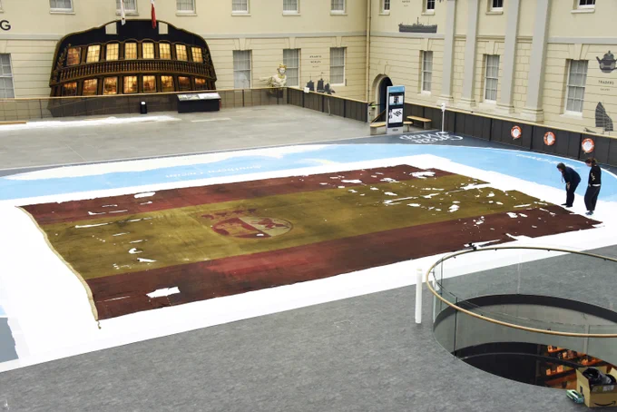 Photo of ensign from the San Ildefonso laid out on the Great Map with two people standing next to it. 