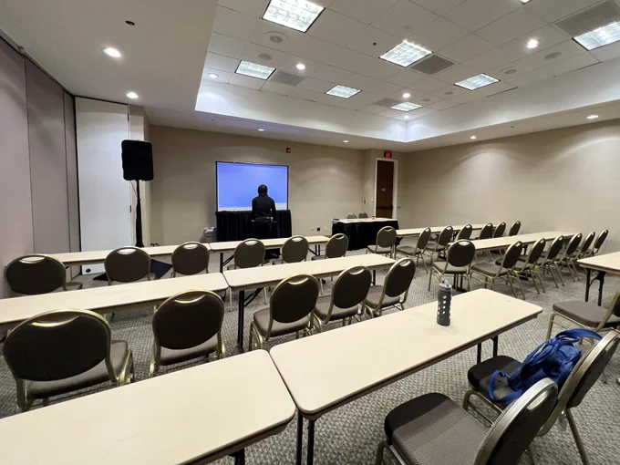 A conference room with long tables and chairs in rows facing a screen