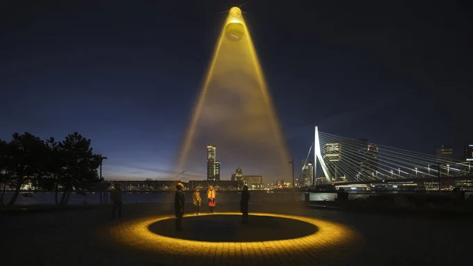 Night time photograph of people standing outdoors within a circle of light being beamed down from the sky.