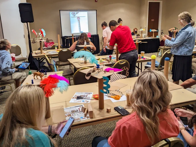 A welcoming space for tinkering with chairs around rectangular tables and people building together.