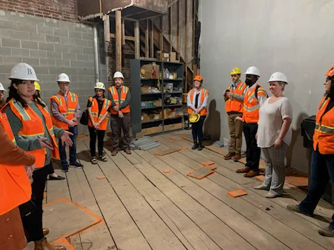 ABA members join PHB and partners to tour the Joyce, a rehab project under construction. People in hard hats and high-viz vests stand in a partially framed room.