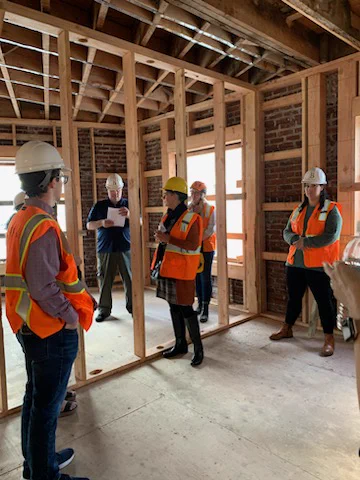 ABA members join PHB and partners to tour the Joyce, a rehab project under construction. People in hard hats and high-viz vests stand in a partially framed room.