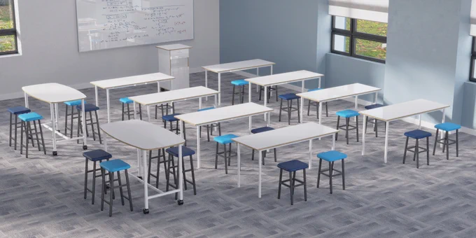 A high school classroom showing 8 rectangular white tables, 2 high tables on wheels and 24 stools of appropriate heights. The stools have upholstered seats for extra comfort. Also visible: a mobile desk for teachers with a lockable drawer, cupboard and space to insert a standard plastic tray or tub.