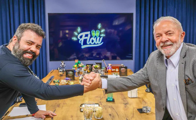 Lula e Igor apertam as mãos. Ao fundo, tv mostra símbolo do Flow podcast