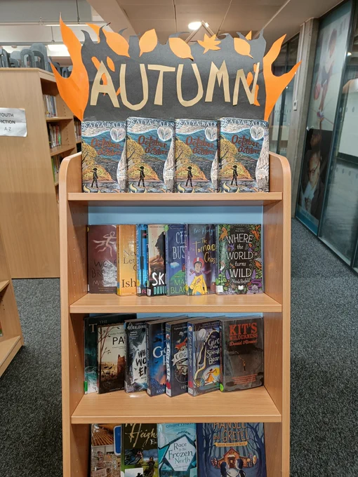 A display of different autumnal books, including four copies of 'October October' across the top. The word 'AUTUMN' is displayed across black and orange paper shaped like flames and leaves.