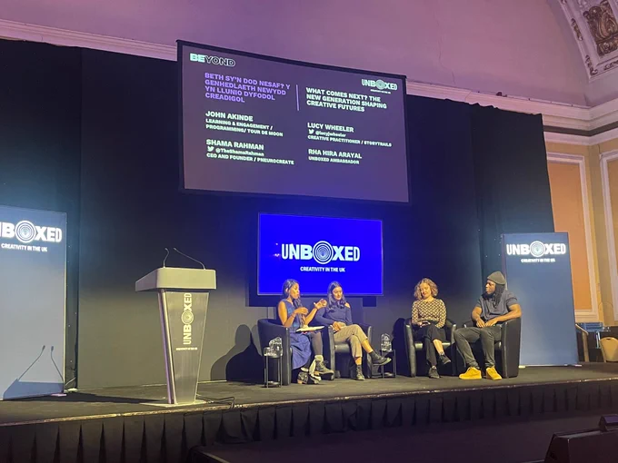 Cardiff City Hall assembly room stage with a seated panel speaking to audience with screens behind then with UNBOXED logo