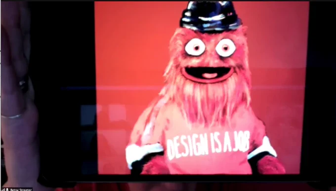 Gritty wearing a shirt that says Design Is A Job