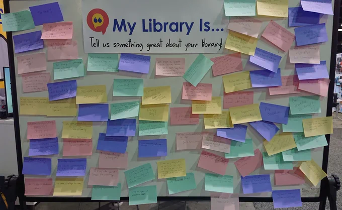 Whiteboard with the My Library Is logo and a lot of sticky notes from booth visitors attached.