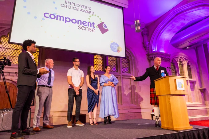 a group of people stand on a stage accepting an award. on a screen behind them it says "employees choice award component sense"