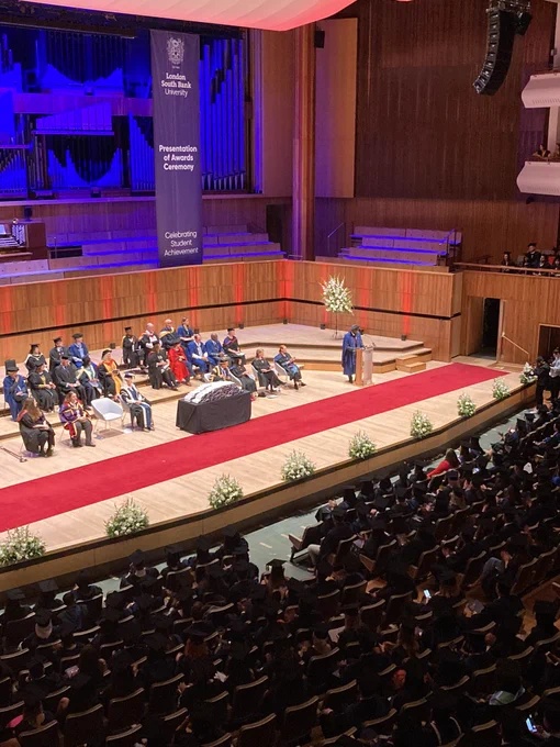 A man stands at a lectern on a stage in academic gowns