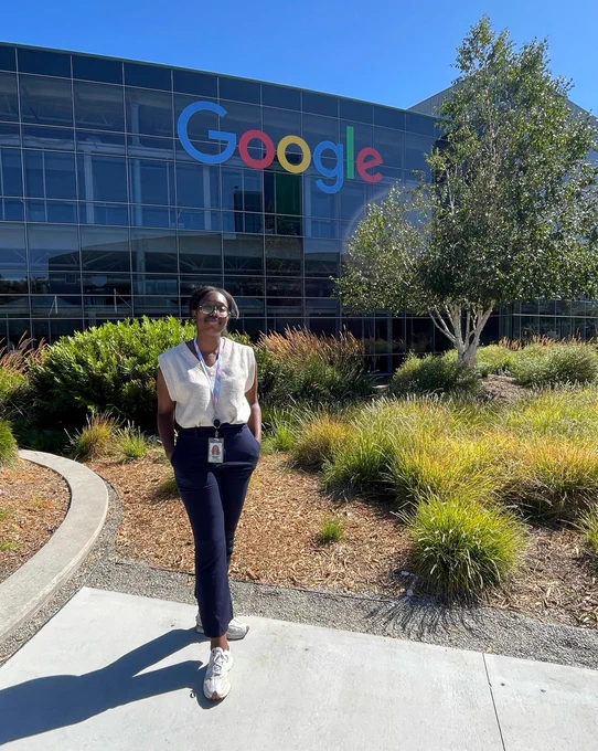 Aurane posing in a white blouse and black pants in front of a Google building.