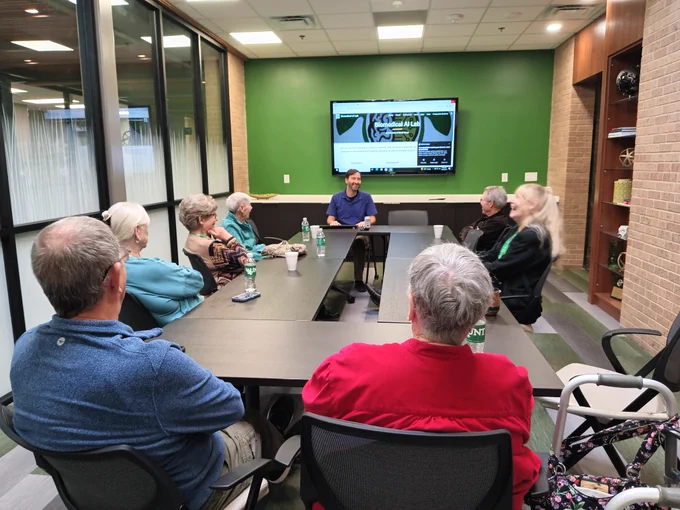 A group of retirees sit around a table in a conference room listening to Dr. Albert.
