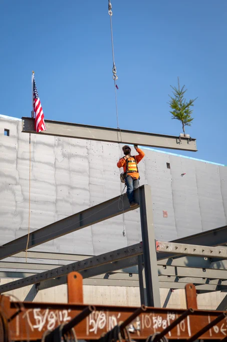 Construction worker stands on top of high beam to lower another beam into place.