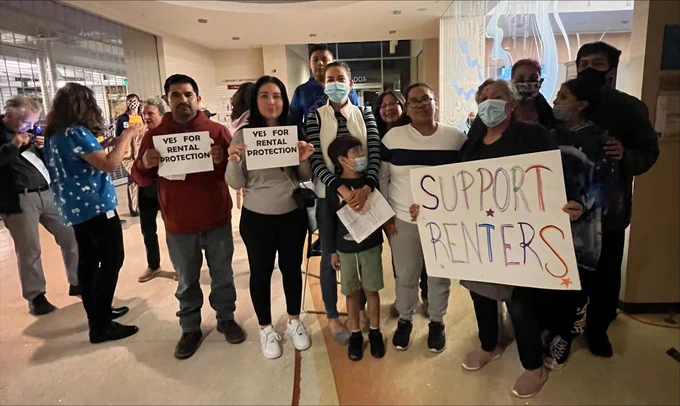 Renters' rights supporters pose for a group photo with signs that say "yes for rental protection" and "support renters."