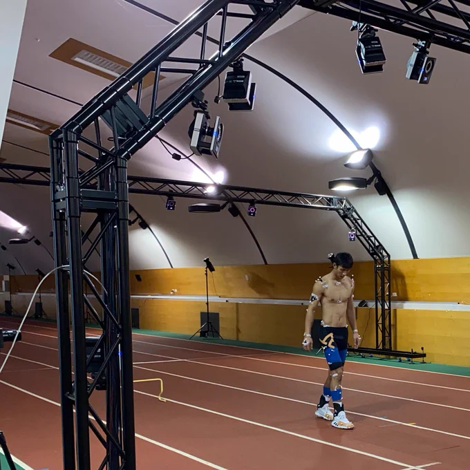 Image shows an athlete with markers attached to their body walking in an indoor athletics track 