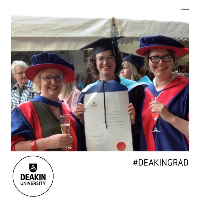 3 women standing in a row. The woman in the middle is wearing academic robes and holding a printed degree. On either side of her are 2 women wearing academic robes holding champagne glasses. All three are smiling.