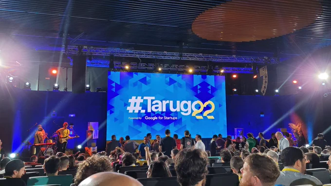 Escenario con pantalla con el logo de Tarugo 22, auditorio lleno de gente, banda con guitarra y teclado a un lado del escenario