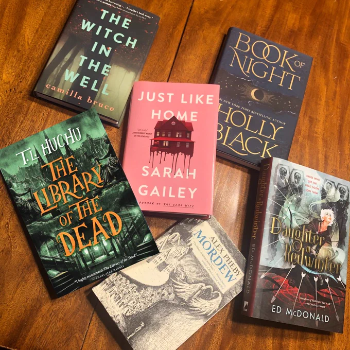 The Witch in the Well by Camilla Bruce, Just Like Home by Sarah Gailey, Daughter of Redwinter by Ed McDonald, Book of Night by Holly Black, The Library of the Dead by T. L. Huchu, and Mordew by Alex Pheby on a wooden table