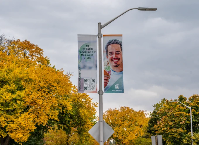 Lamp post banner with a Spartan holding an ice cream cone that says "Try every flavor at the Dairy Store"