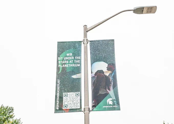 Lamp post banner that has a photo of the Planetarium on it and says "Sit under the stars at the Planetarium" 