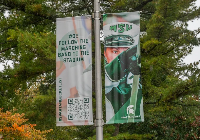 Lamp poster banner with a Spartan Marching Band member on it that says "Follow the Marching Band to the Stadium"