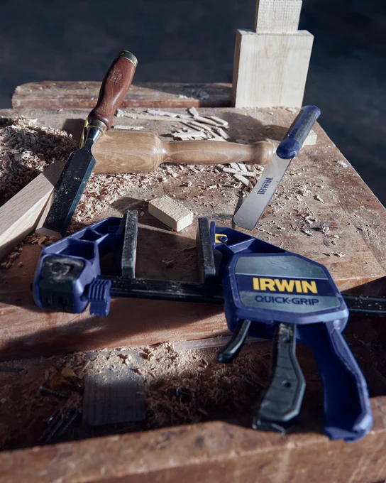 An image of an IRWIN® Quick-Grip Clamp resting on a woodworking station. 
