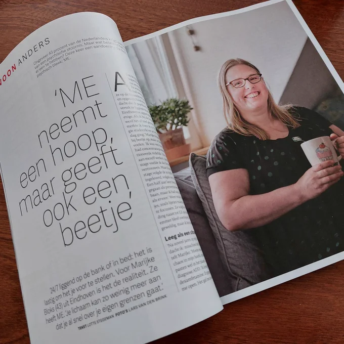 afbeelding van de eerste twee pagina’s en de portretfoto van Marijke, die een interview gaf over ME aan Quest psychologie. Op de linkerpagina de kop “ME neemt een hoop, maar geeft ook een beetje”, op de rechterpagina een foto van Marijke, met lichtbruin lang haar en een bril, die in de bank zit met een mok thee of koffie en lacht naar de camera.
