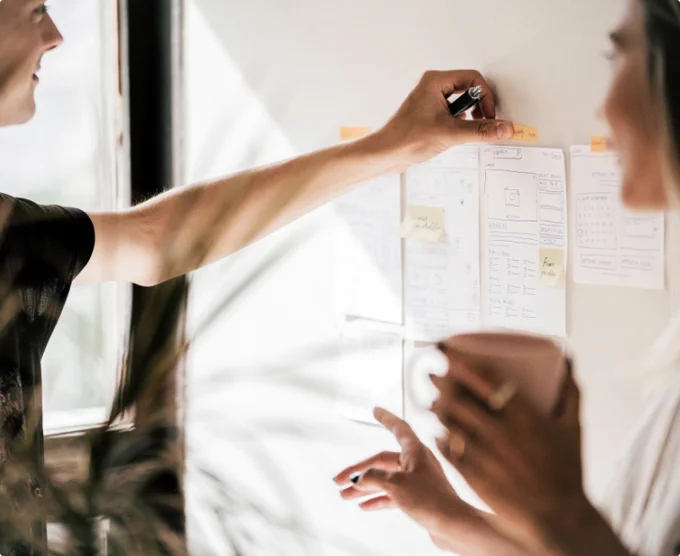 Two people placing paper notes onto a white wall.