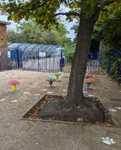 Photo of school entrance with colourful toadstools for the children to play on and animal footprints leading around the tree.