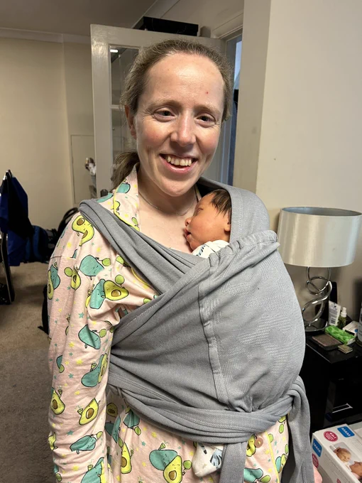 Lora stood wearing Fraser on her front in a sling.