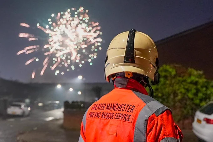 Firefighter in uniform and helmet looks at firework in the distance.