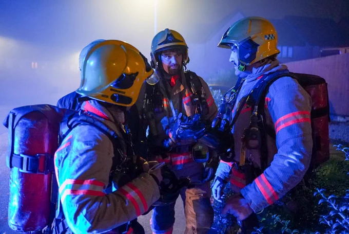 Three firefighters in uniform illuminated by blue light.