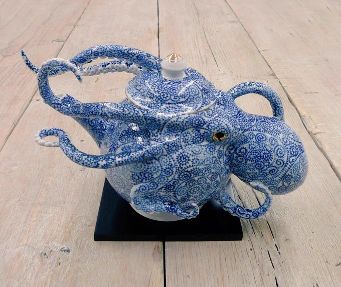 Photograph featuring a blue and white teapot on a wooden floor, the ceramic teapot is in the shape of an octopus, with head to the right and legs to the left