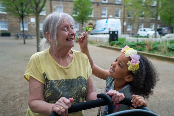 Image of young girl and older woman pushing a pram and smiling together.