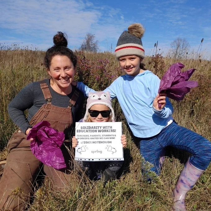 Woman and two children out in field showing their sign of support for education workers.