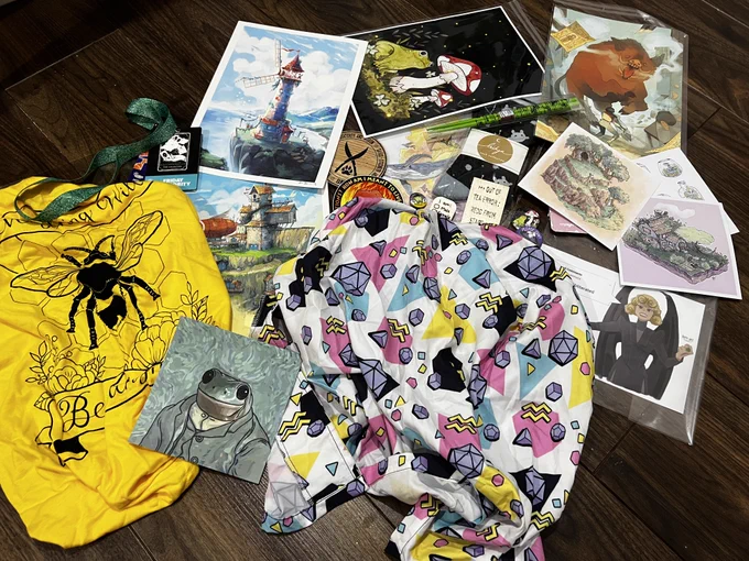 A collection of art prints, a shirt, tshirt badges and chopsticks messily arranged on a wooden floor