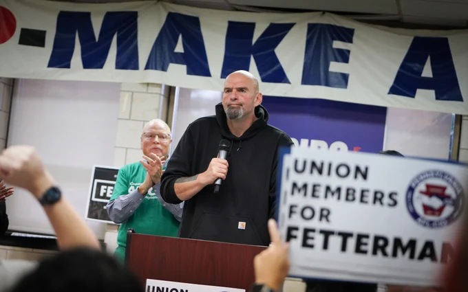 Me speaking in the union hall as a member of the audience holds up a Union Members for Fetterman sign.