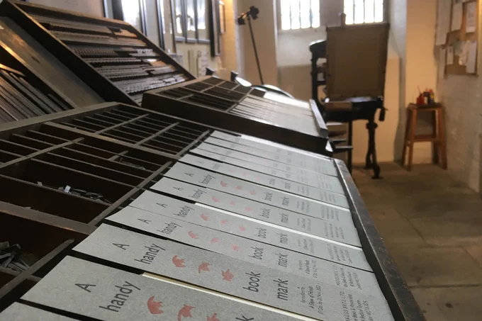 A line of printed pamphlets, featuring printer's fists, laid out on an old fashioned printing press.