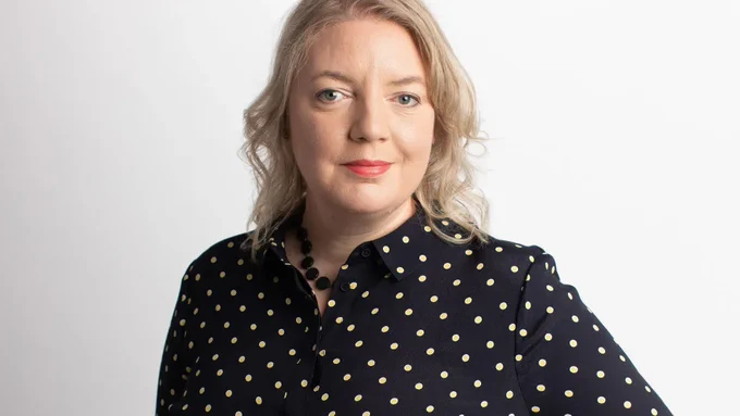 Photo of Claer Barrett smiling at the camera. She is wearing a black shirt with yellow dots. Photo credit: Charlie Bibby FT