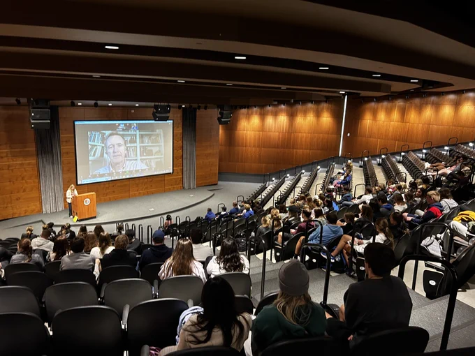 Creighton Dean Fellow students sitting in Creighton's Harper Auditorium facing a projected zoom screen with Dr. Chris Lowney