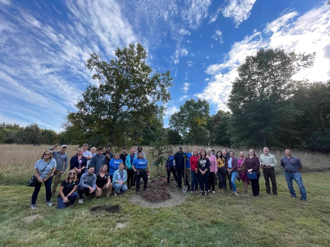 Group photo of people standing outside in front of trees.