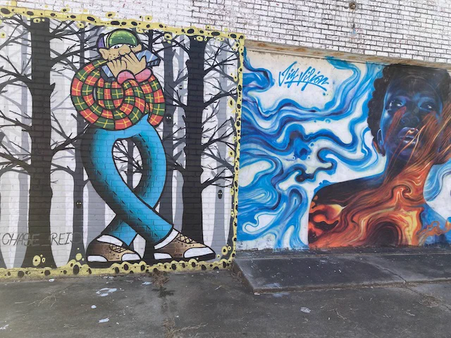 Street art, paintings on building in Clarksdale, Mississippi, USA, colourful character playing harmonica in a woodland setting, beside woman singing and looking up in an abstract red and blue swirly design.