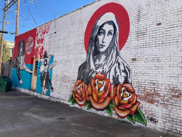 Street art wall painting in Clarksdale, Mississippi, USA, painting by Austin Britt, based on Mystical Rose. Woman in front of red circle and behind three roses.
