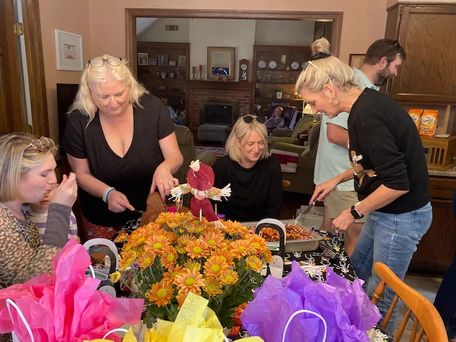 American family celebrating birthdays with flowers, presents, and cakes in the kitchen of a home in Memphis, Tennessee, USA. People having fun, smiling, eating, with orange daisy mums and red, yellow, purple, tissue paper poking out of gift bags on the table.